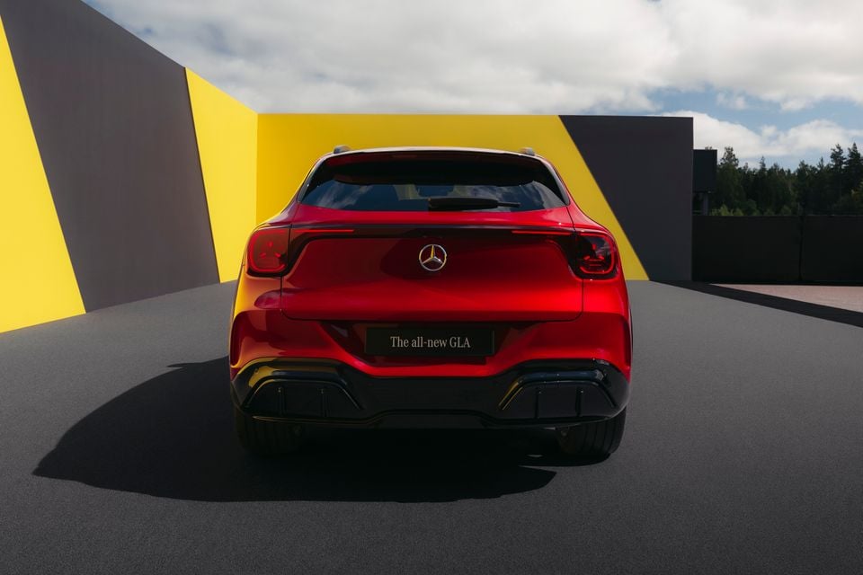 The rear of a red Mercedes-Benz GLA SUV, shown in a styled outdoor setting with yellow and grey geometric backdrops.