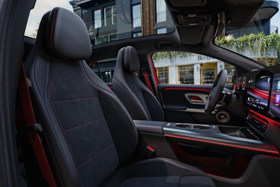 Interior of a 2027 Mercedes-Benz GLA showing dark Alcantara front seats with red stitching, a large infotainment touchscreen, steering wheel, and red ambient lighting