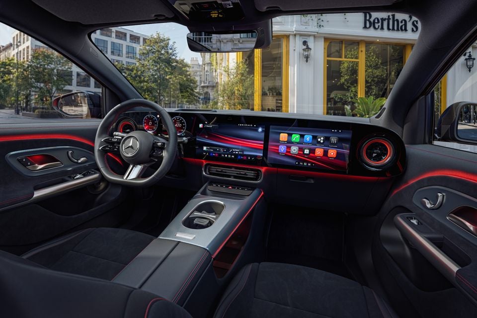 Interior of a Mercedes-Benz GLA showing the dual widescreen display, sport steering wheel, red ambient lighting, and dark upholstery with red stitching