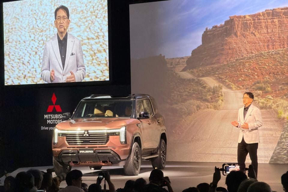 A Mitsubishi Pajero SUV unveiled on stage at a launch event, with a Mitsubishi Motors executive presenting beside it and the Pajero name visible on the front bumper
