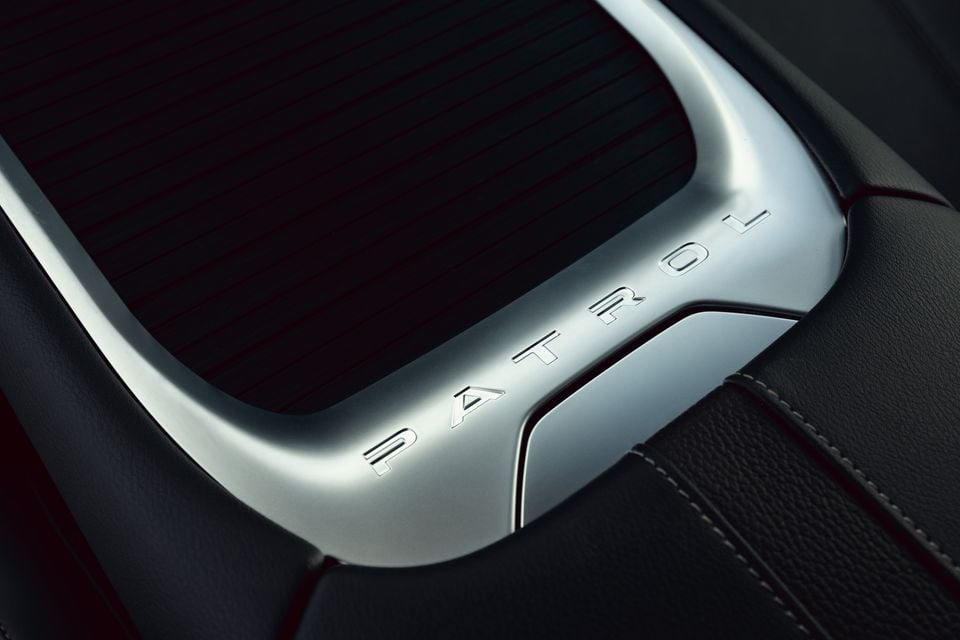 Close-up of the 'Patrol' nameplate embossed on a silver interior trim panel of a Nissan Patrol, surrounded by dark leather upholstery.