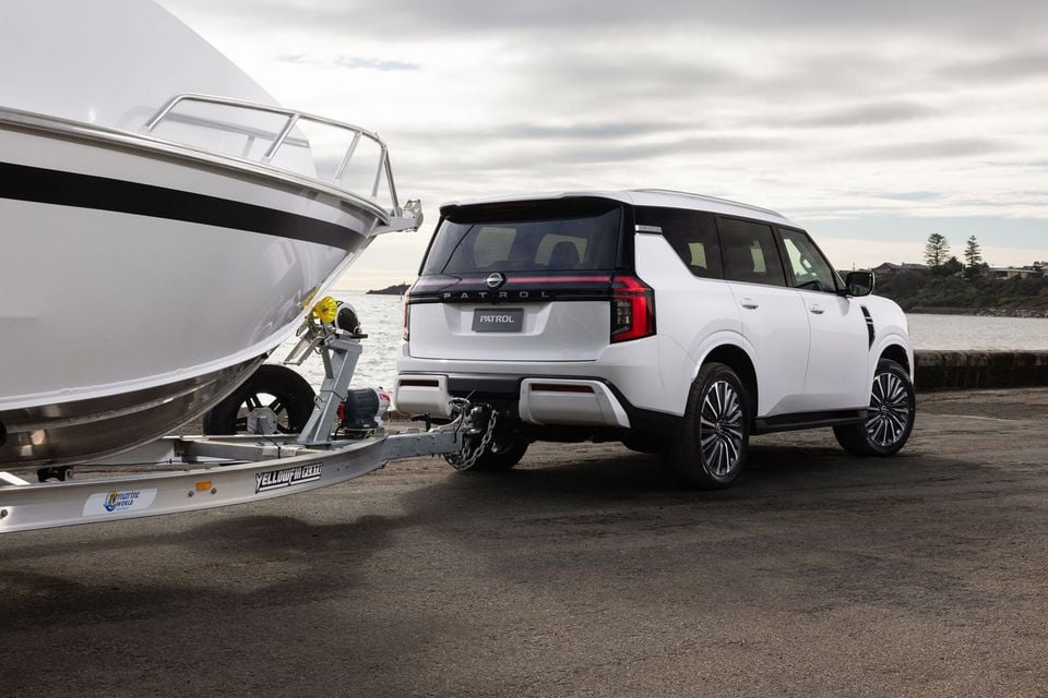 White Nissan Patrol large SUV seen from the rear, towing a boat on a trailer near a waterfront