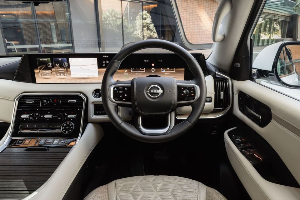 Interior of a Nissan Patrol Y63 showing the steering wheel, dual-screen infotainment and digital instrument cluster, and cream leather upholstery with right-hand drive layout.