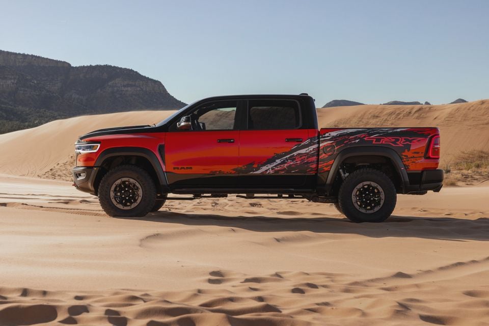 A red and black Ram 1500 TRX crew cab ute seen from the side, parked on sand dunes with rocky mesas in the background