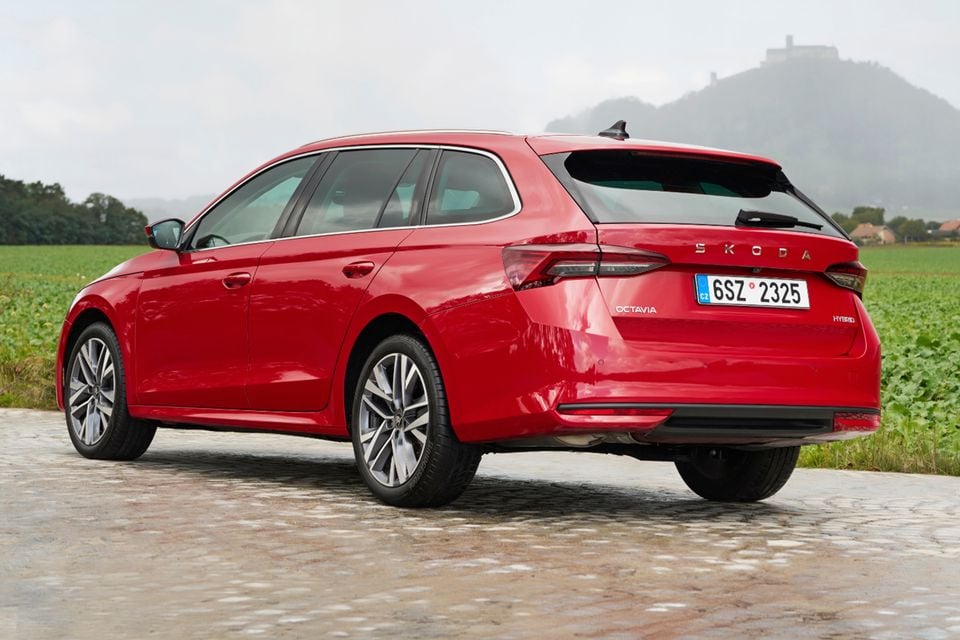 A red Skoda Octavia wagon parked on a cobblestone road, seen from the rear quarter with a hill and castle in the background