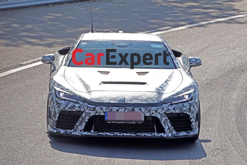 A camouflaged Toyota GR GT prototype supercar seen from the front on a road during testing