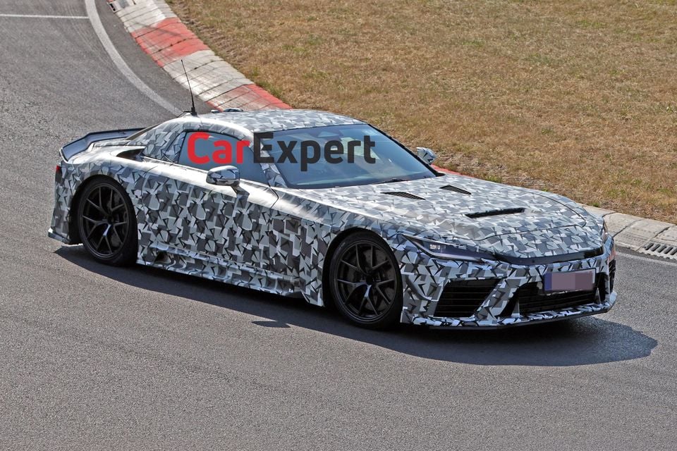 A camouflaged Toyota GR GT prototype coupe seen from the front-side angle on a racetrack