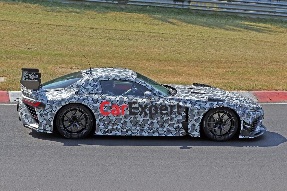 A camouflaged Toyota GR GT3 sports car prototype seen from the side on a race track, featuring a large rear wing and wide-body aero kit