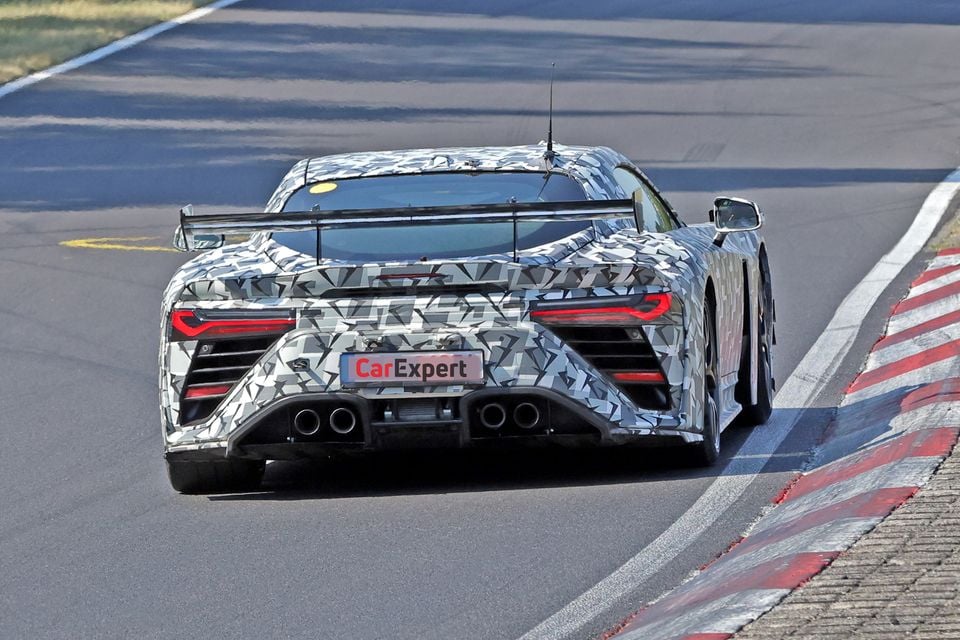 A camouflaged Toyota GR GT RS supercar prototype seen from the rear, driving on a race track, showing a large rear wing and quad exhausts