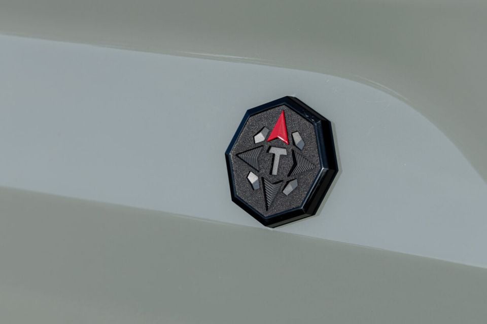 Close-up of the Toyota Tundra Trailhunter badge on the exterior of a light-coloured vehicle, featuring an octagonal dark emblem with a red arrow and geometric shapes.
