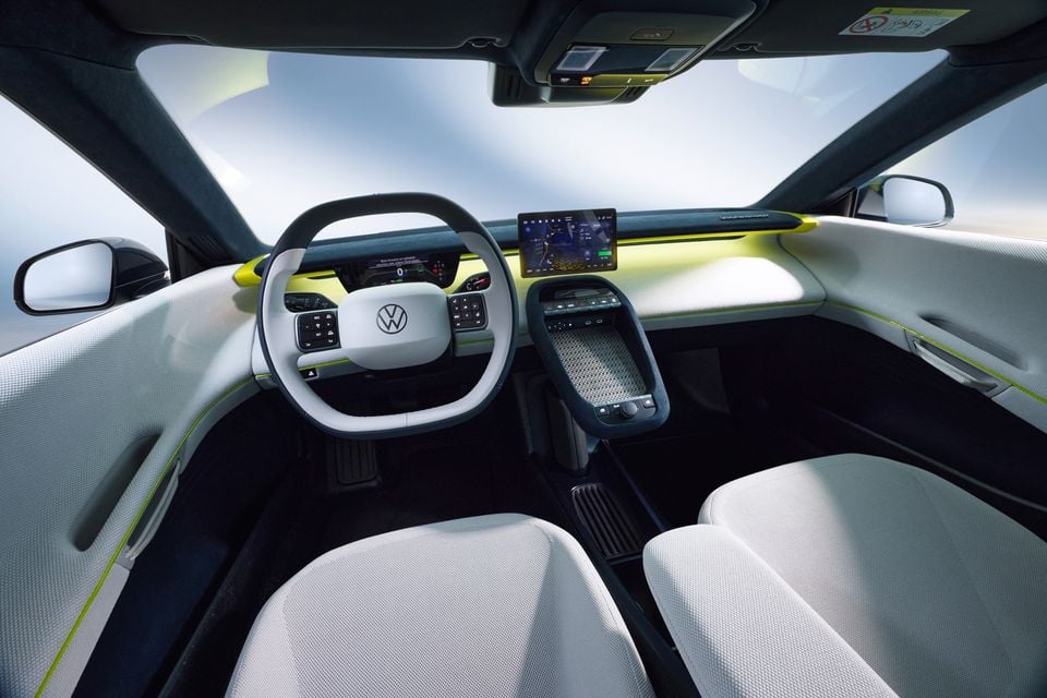 Interior of a Volkswagen concept car showing a round steering wheel with VW logo, digital instrument cluster, central touchscreen infotainment display, and white and yellow-green cabin trim
