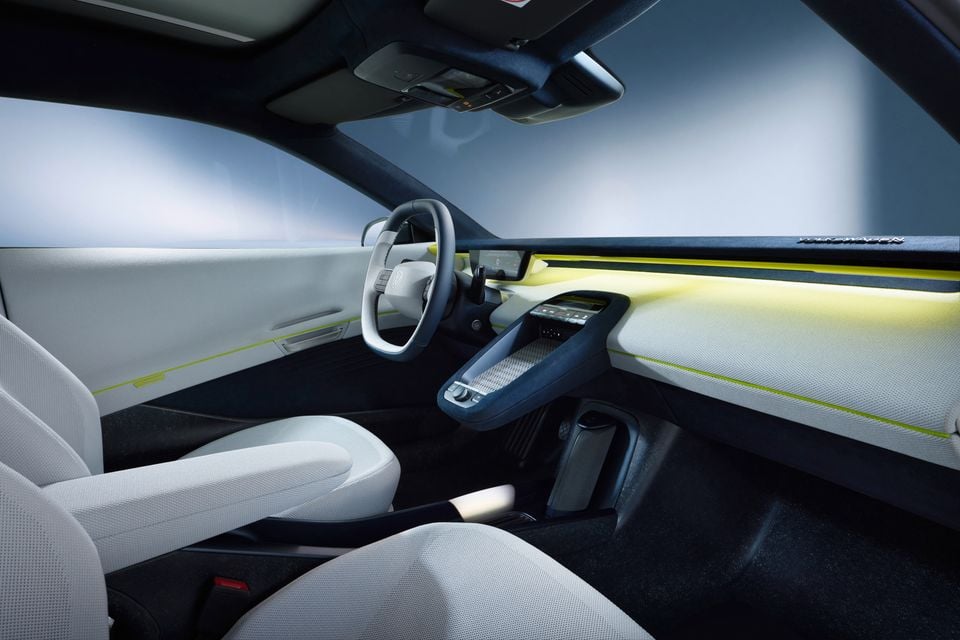 Interior of a Volkswagen concept car showing white fabric seats, a rounded steering wheel with the Volkswagen logo, and a minimalist dashboard with yellow-green ambient lighting accents