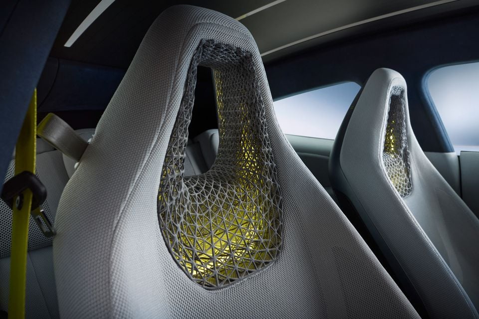 Close-up of a concept car's front seats featuring lattice-structured mesh headrests with yellow illuminated inner layers, viewed from the rear cabin