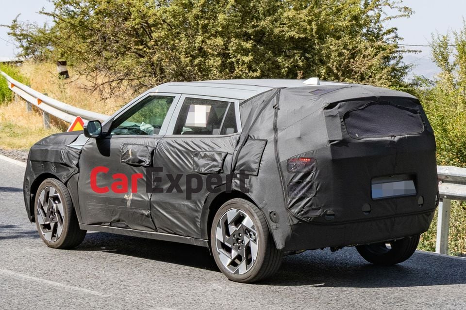 A camouflaged Hyundai Kona SUV prototype seen from the rear three-quarter angle on a public road during testing