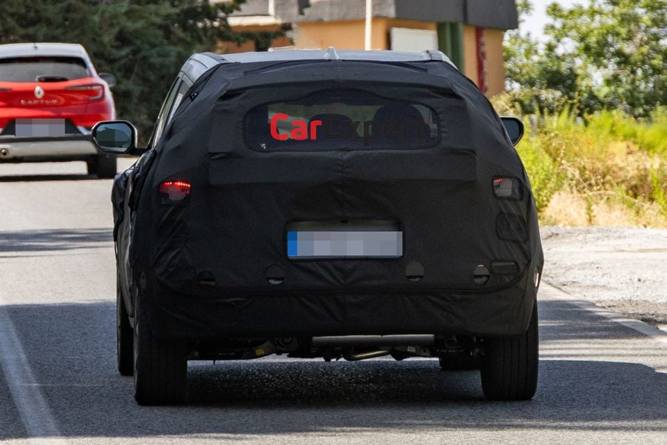 A camouflaged Hyundai Kona SUV prototype seen from the rear while driving on a public road during testing