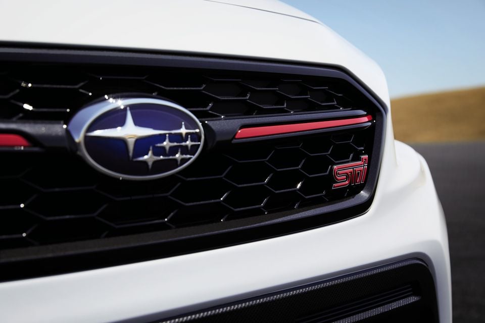 Close-up of the front grille on a white Subaru WRX STI, showing the Subaru badge and red STI emblem on a black honeycomb grille