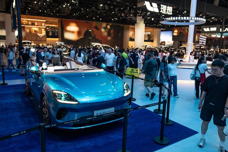 A light blue Arisataland GX7 convertible on display at the Chengdu Motor Show, surrounded by crowds of visitors browsing various car brand stands.