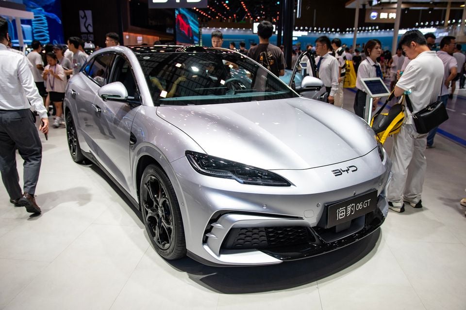 A silver BYD Seal 06 GT on display at a motor show, seen from the front-side angle, surrounded by attendees