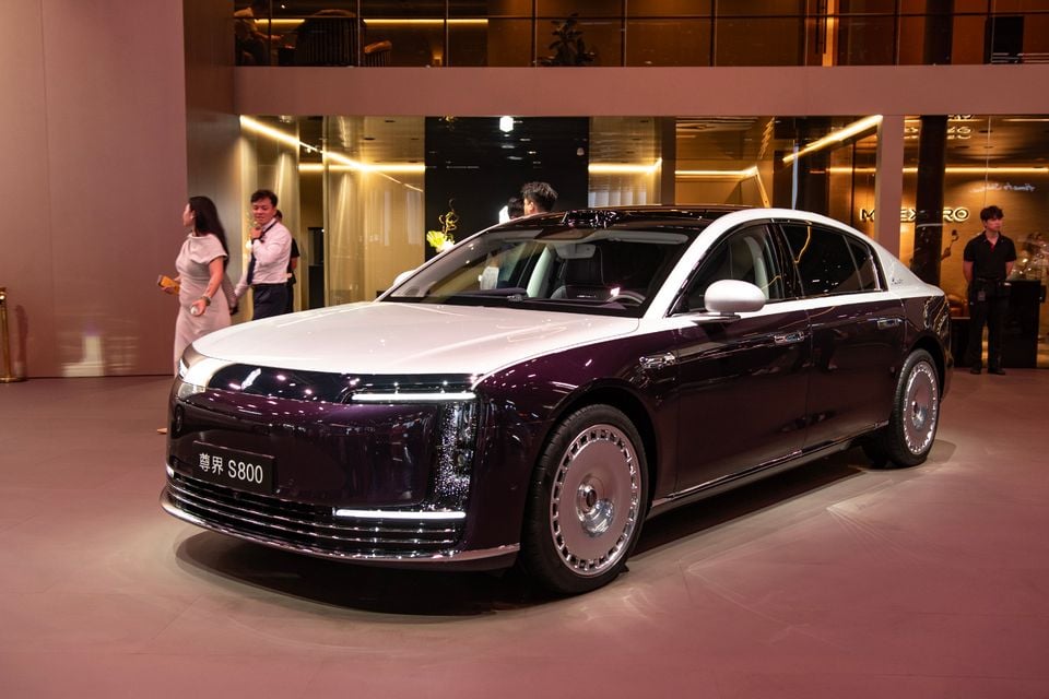 A Maextro S800 luxury sedan in two-tone purple and white, seen from the front-side at an indoor motor show event