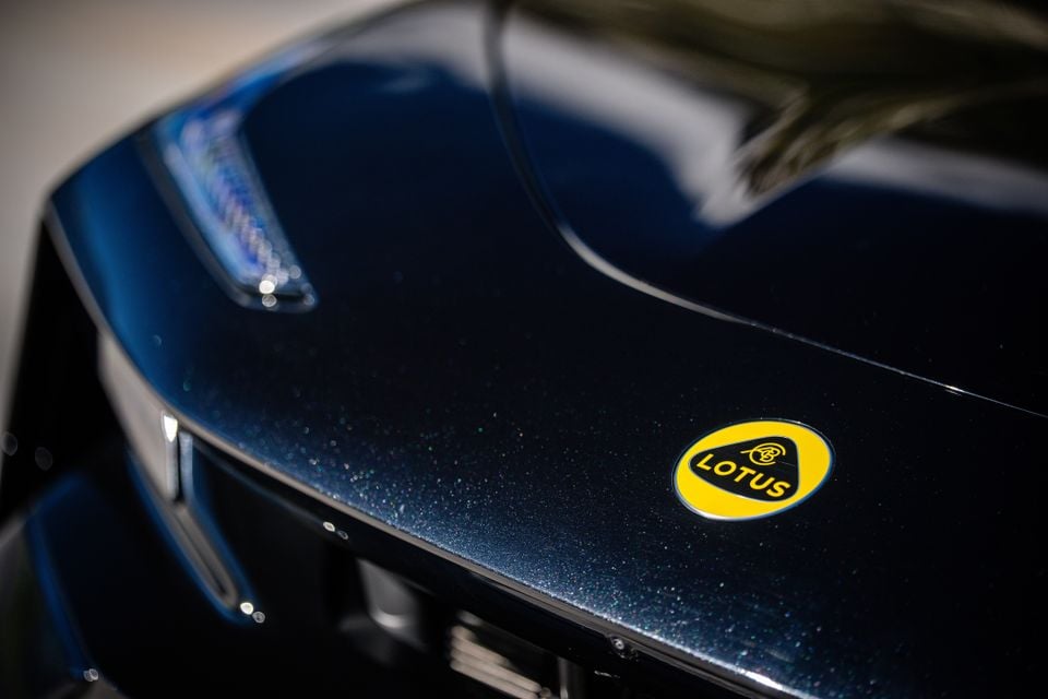 Close-up of the yellow Lotus badge on the dark blue bonnet of a 2027 Lotus Eletre X, with a headlight visible to the side