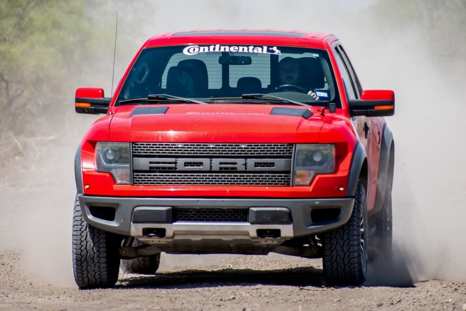 A red Ford F-150 SVT Raptor ute driving on a dirt track, kicking up dust, seen from the front