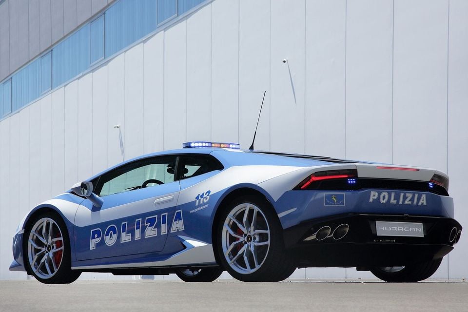 A Lamborghini Huracan coupe in Italian Polizia livery, blue and white with police lights, seen from the rear three-quarter angle