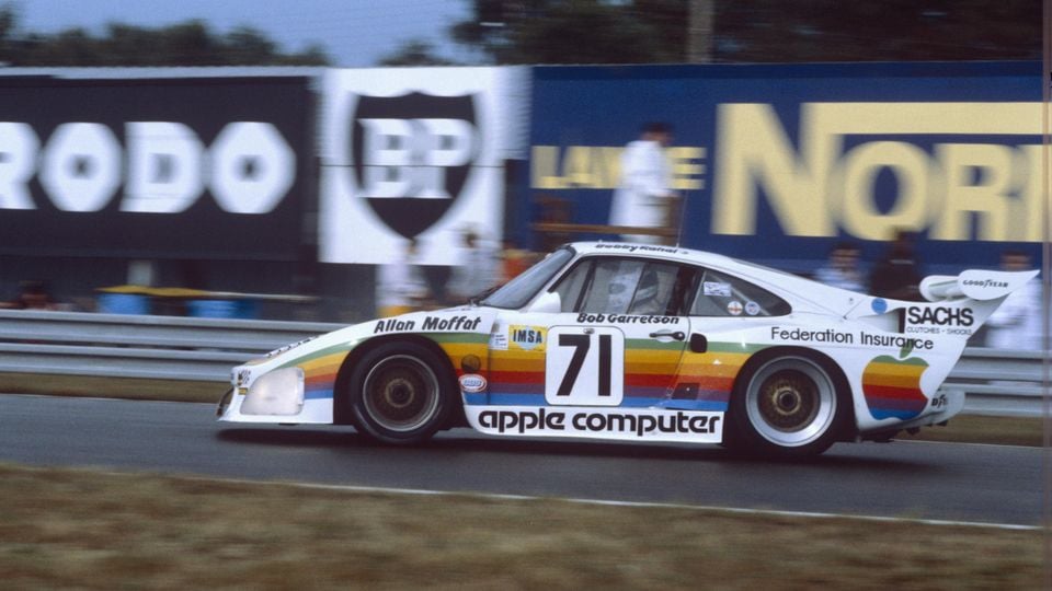 A Porsche race car numbered 71 with Apple Computer sponsorship livery and rainbow stripes, driven by Allan Moffat and Bob Garretson, racing on a circuit