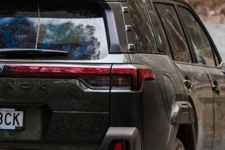 Close-up of the rear tail light and badging of a muddy dark-coloured SUV, seen from behind, with a second similar SUV alongside