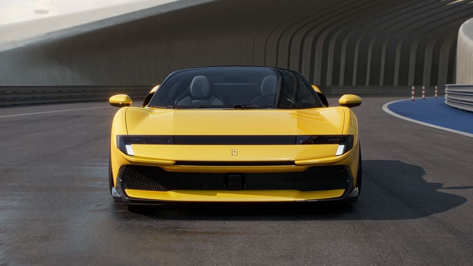 A yellow Ferrari supercar seen from the front, parked on a racetrack with concrete barriers in the background