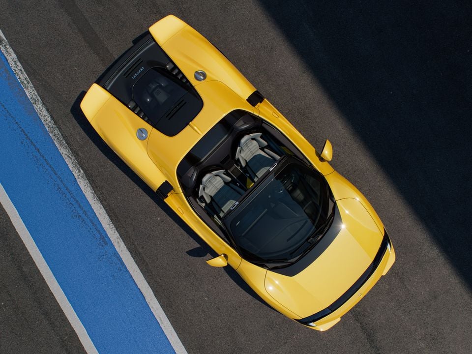 A yellow Ferrari Testarossa Spider seen from directly above on a race track, with the open-top cabin and light-coloured seats visible