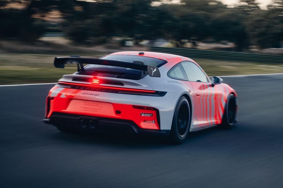 A Porsche 911 GT3 in white and red livery seen from the rear while driving on a race track