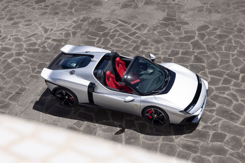 A silver Ferrari supercar seen from above, parked on a cobblestone surface, with red interior seats visible through the open targa-style roof