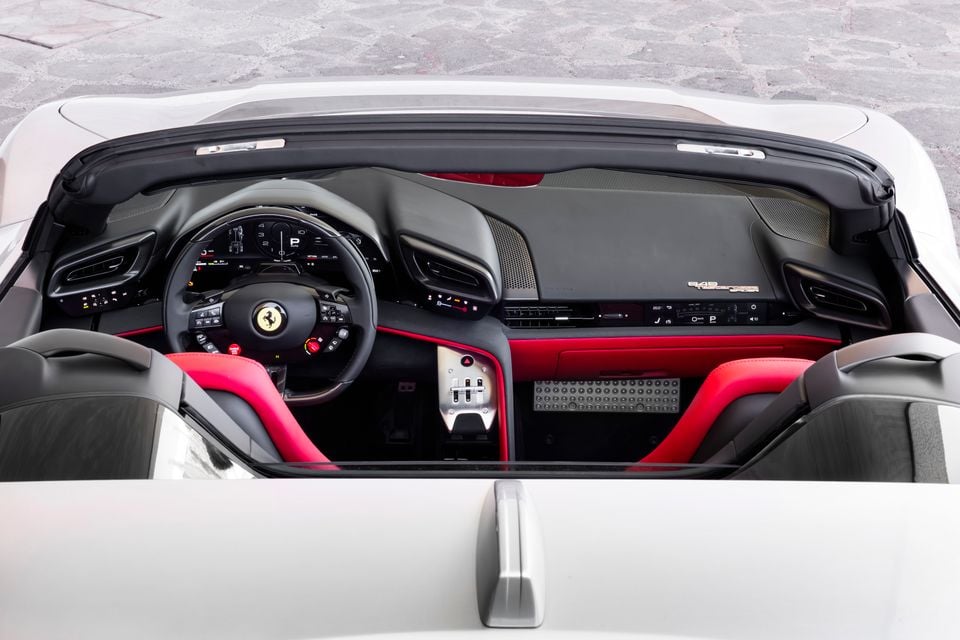 Ferrari interior viewed from above showing the steering wheel with prancing horse badge, red and black dashboard, digital instrument cluster, centre console and open-top cabin