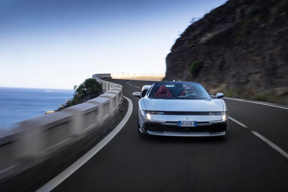 A white Ferrari open-top supercar driving along a coastal cliff road, seen from the front