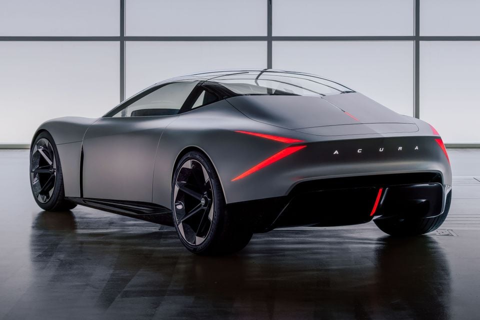 Acura Nexera Vision concept car seen from the rear three-quarter angle, finished in matte grey with sharp red tail light accents, displayed indoors on a polished floor.