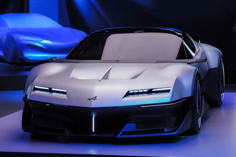 Carro-conceito Silver Alpine A310 Vision visto de frente em um leve ângulo, exibido sob iluminação azul ao lado de um carro coberto