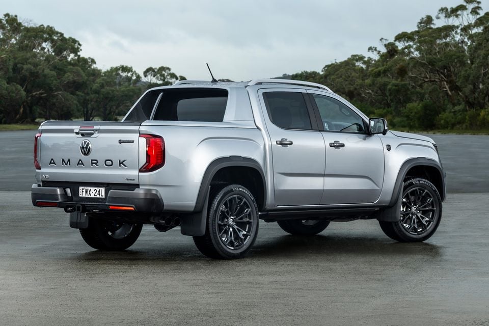 A silver Volkswagen Amarok V6 dual-cab ute seen from the rear three-quarter angle, parked on a open surface with trees in the background