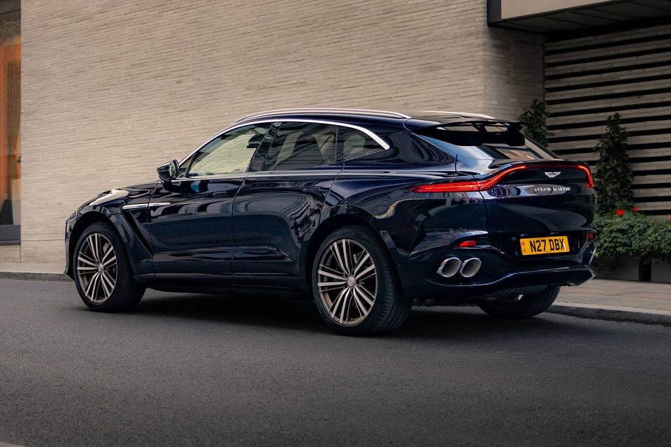A dark blue Aston Martin DBX GT SUV parked on a street, seen from the rear quarter angle.