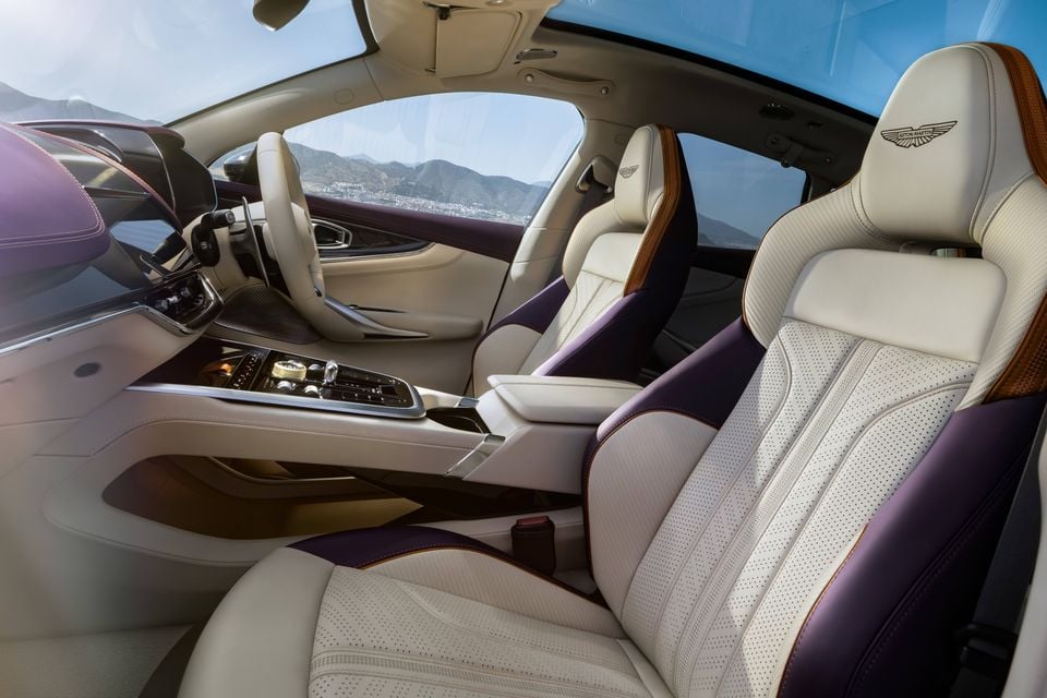 The cream and purple leather interior of an Aston Martin DBX, showing the front seats, steering wheel and centre console.
