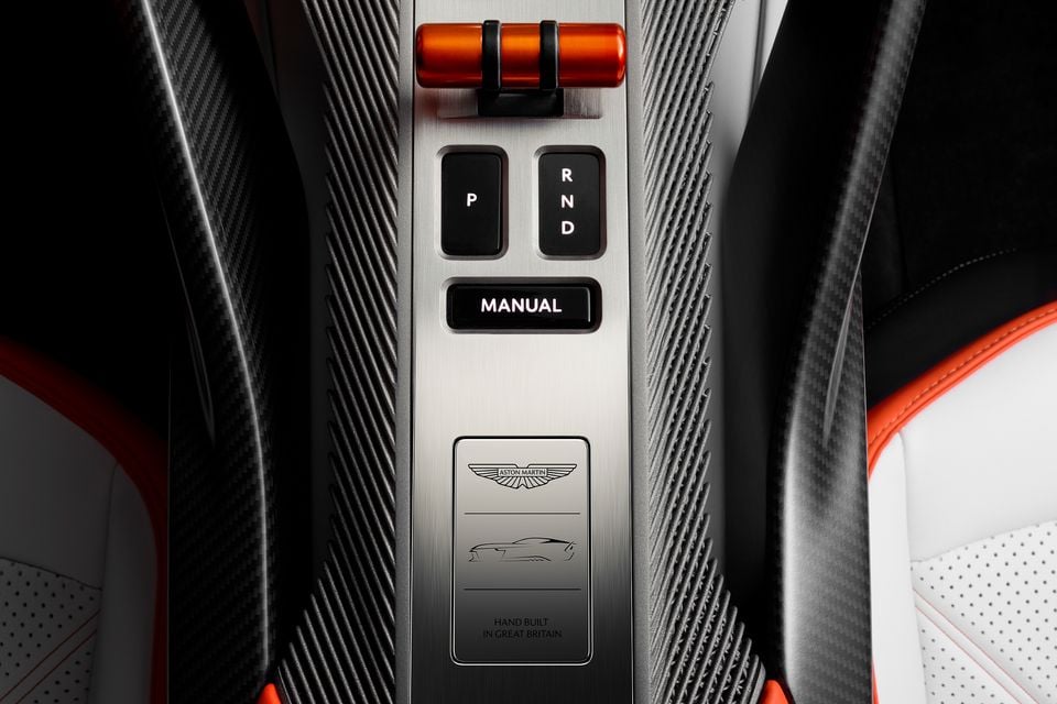 Aston Martin Valen centre console showing gear selector buttons (P, R, N, D, Manual) with an orange rotary control, carbon fibre trim, and an engraved 'Hand Built in Great Britain' plaque