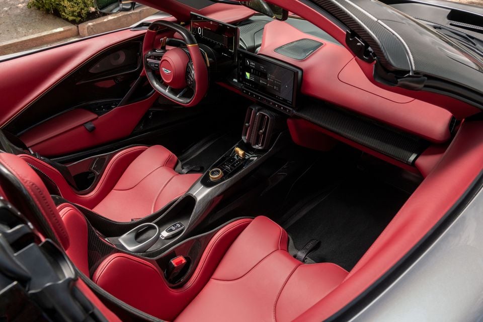 Red leather interior of an Aston Martin Valhalla Spider, showing carbon-fibre bucket seats, steering wheel, digital screens and centre console
