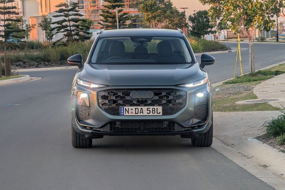 A dark grey Audi Q3 SUV seen from the front, with headlights on, parked on a suburban street in Australia.