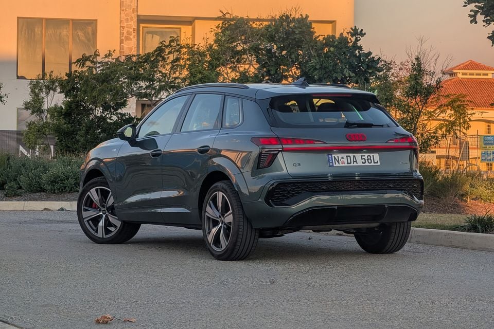 An Audi Q3 SUV seen from the rear three-quarter angle, finished in dark grey, parked in a suburban street at dusk