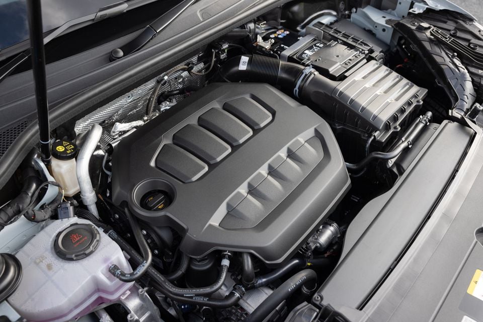 The engine bay of an Audi Q3, showing the turbocharged four-cylinder engine with a grey plastic cam cover and surrounding components including fluid reservoirs and air intake.