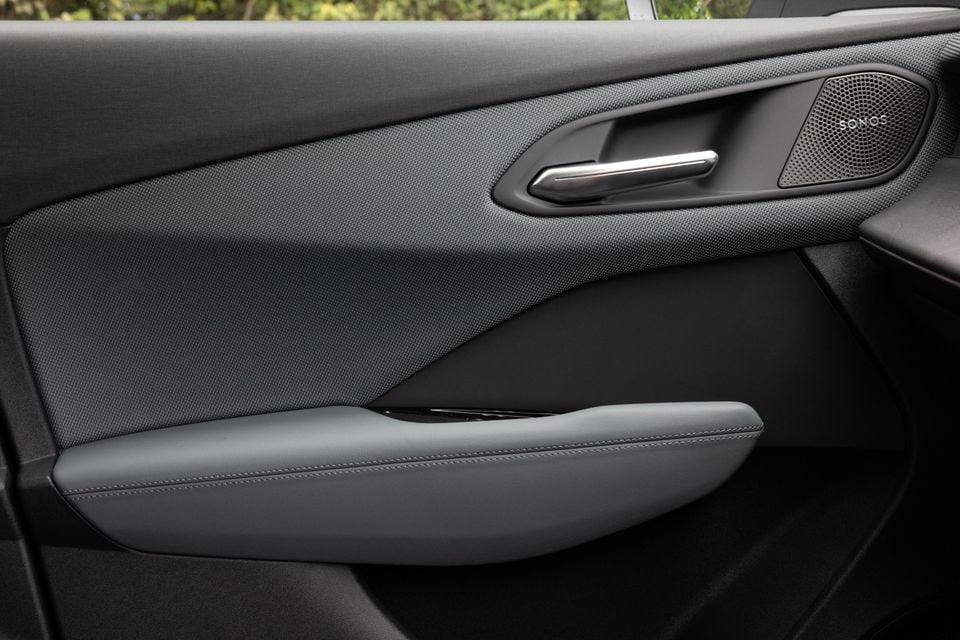 Car door panel interior showing a Sonos speaker, chrome door handle, textured trim and padded armrest