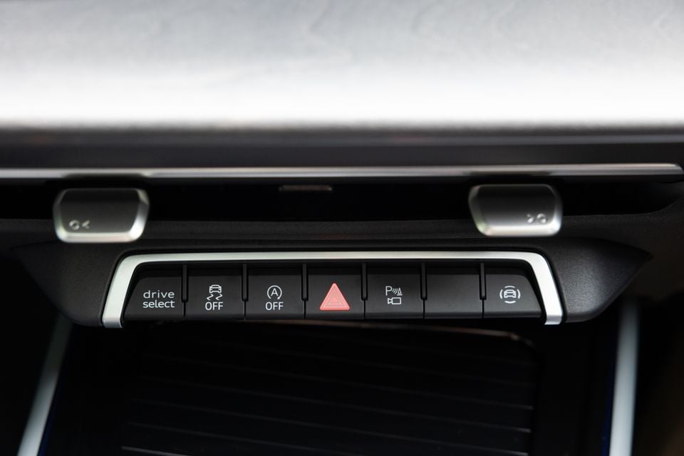 Close-up of the centre console button panel in an Audi Q3, showing drive select, traction control off, auto start-stop off, hazard lights, lane assist, and park assist controls