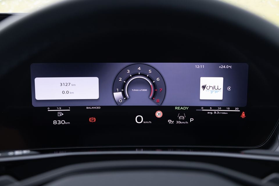 Digital instrument cluster of an Audi Q3 showing a tachometer, speedometer reading 0 km/h, odometer at 3127 km, 830 km range, average fuel consumption of 9.3L/100km, and a radio station display
