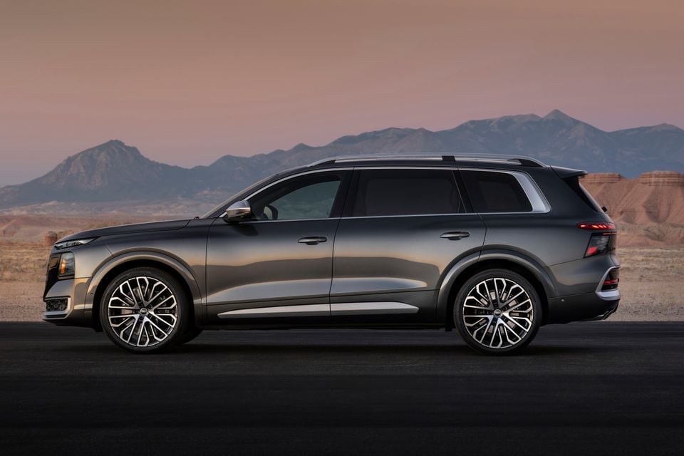 A grey 2027 Audi SQ9 large SUV seen from the side, parked in a desert landscape at dusk with mountains in the background.