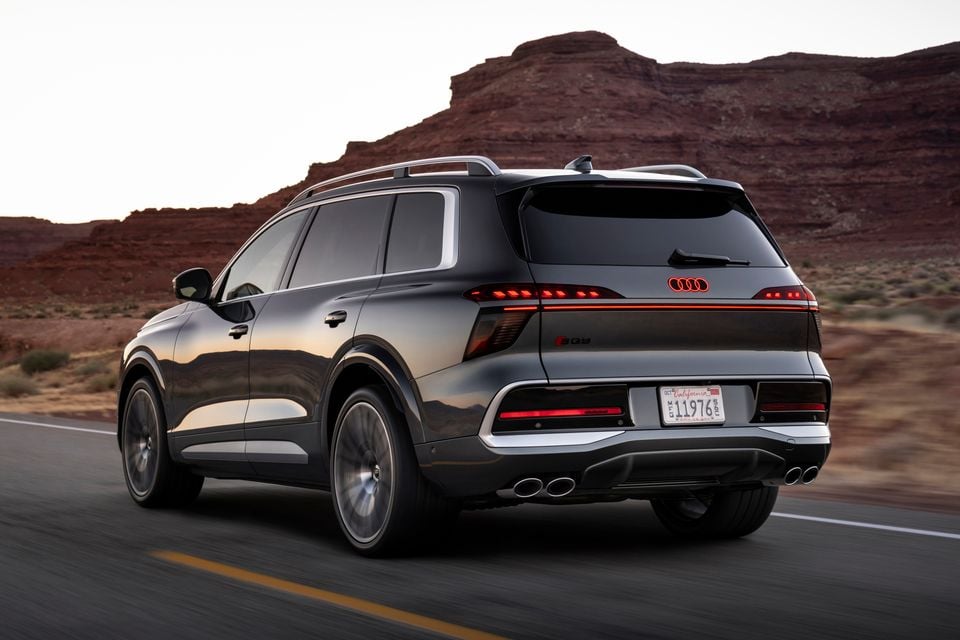 An Audi SQ9 SUV seen from the rear three-quarter angle, driving on a road with red rock formations in the background