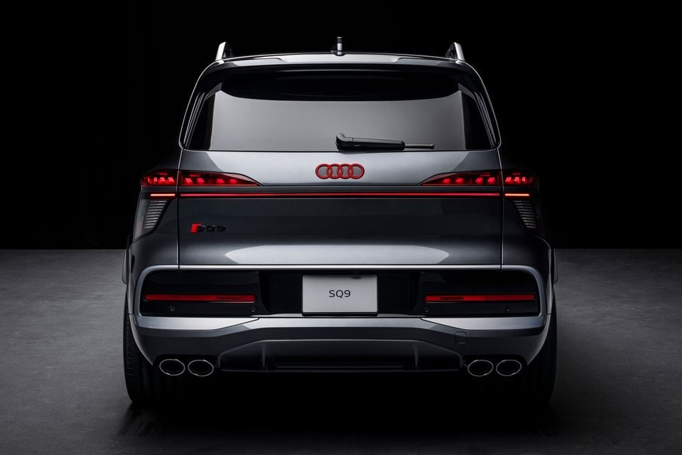 Rear view of an Audi SQ9 SUV in grey, shown against a dark studio background with quad exhaust tips visible